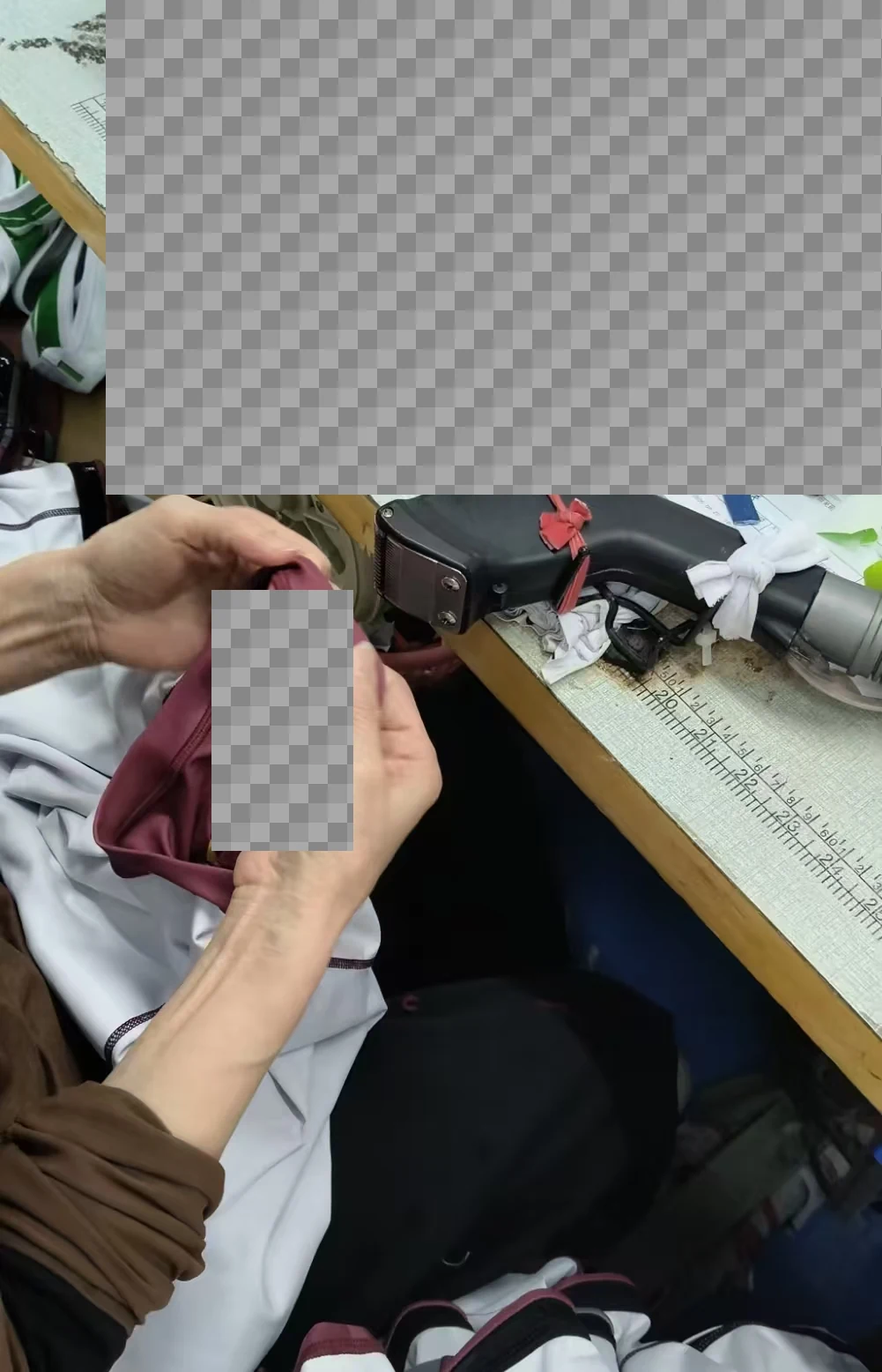An operator handling a garment edge at a workbench; paperwork and customer markings are obscured.