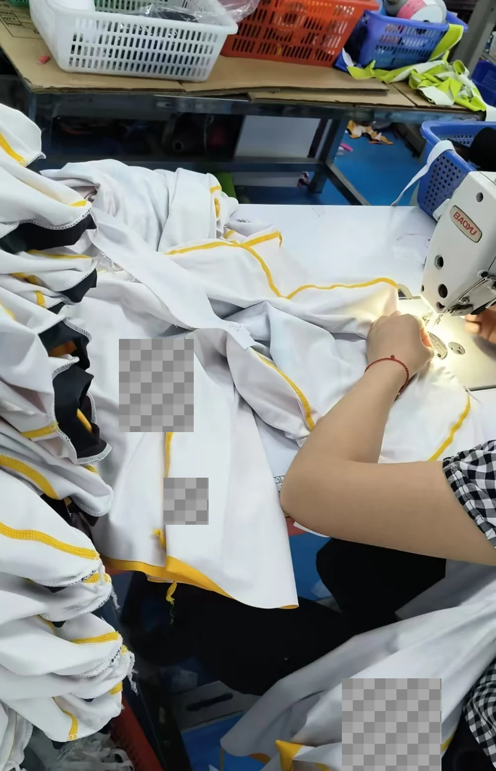 An operator working with a white garment with contrasting yellow seams at a sewing machine.