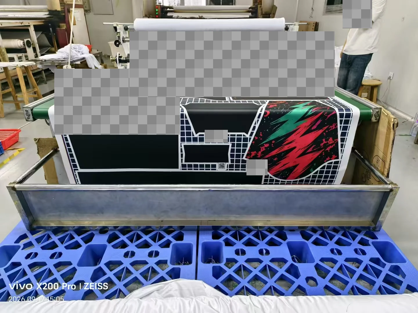 Printed garment-shaped panels on roll-processing equipment; customer artwork and codes are obscured.